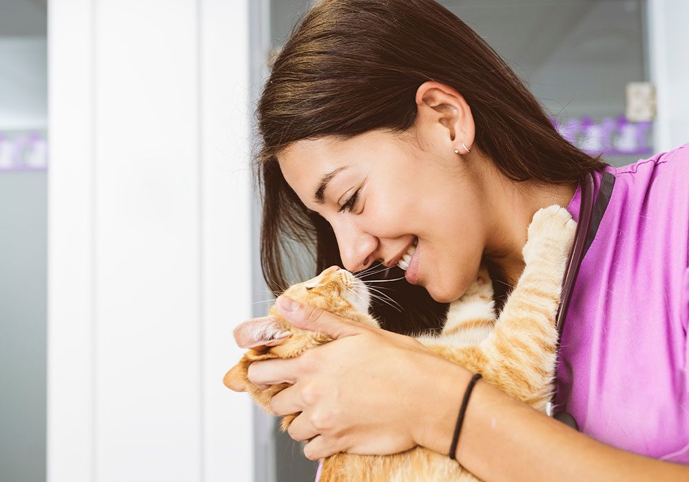 female veterinarian smiling while holding orange tabby cat
